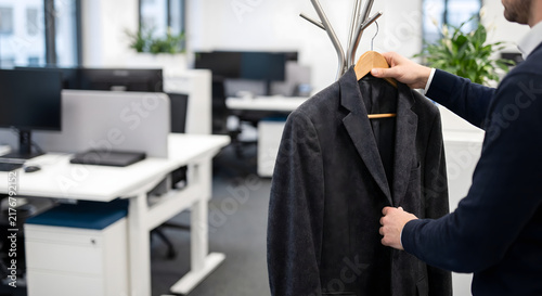 Person hanging a wool winter blazer on a wooden coat rack in modern office