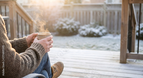 Person holding a steaming cup of coffee on a frost covered wooden deck in the morning