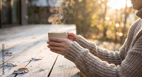 Hands holding a steaming mug on a wooden table in golden morning sunlight
