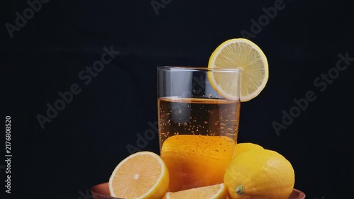 Fresh lemon juice being glass with lemons on table black background