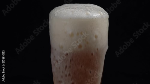 Closeup hoppy unfiltered beer foaming in glass. Foam alcohol beverage flowing down clean goblet on black background. 
