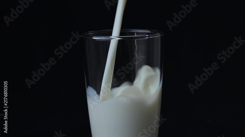 Pouring milk into glass on black background
