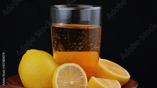 Fresh lemon juice being glass with lemons on table black background