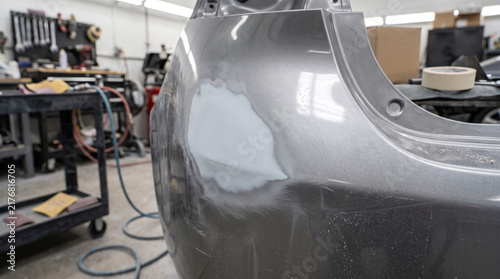 Car panel with applied body filler being sanded in a professional repair shop.