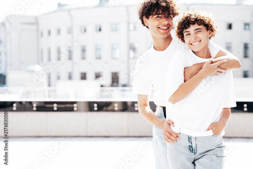 Young smiling beautiful woman and her handsome boyfriend in casual summer white t-shirt and jeans clothes. Happy cheerful family. Female having fun. Couple posing in street at sunny day