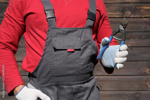 Foto Construction worker in red shirt and gray overalls holding blue bolt cutters wit
