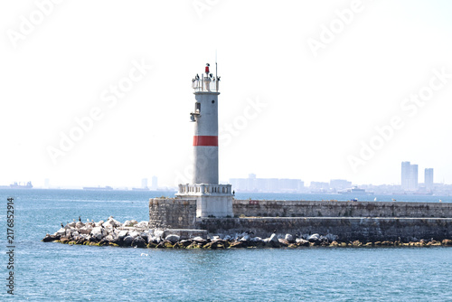 White lighthouse with red stripes. Marine traffic control equipment. A guide for ships. The sea, the sky, and the lighthouse. Copy space, blank, empty. No people, nobody. Horizontal photo.