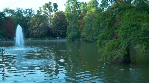 A serene scene featuring a water fountain spraying into a lake surrounded by lush green trees in Madrids Retiro Park. Perfect for travel and wellness content.