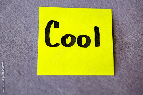 Bright yellow sticky note with handwritten word Cool on grey felt background, positive assessment concept