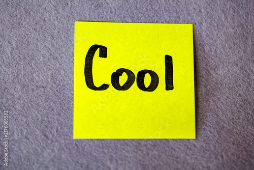 Bright yellow sticky note with handwritten word Cool on grey felt background, positive assessment concept