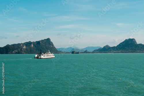 Fotografie Passenger Ferry Crossing Turquoise Sea Below Rugged Mountain Islands
