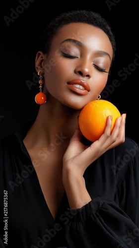 Woman holding orange fruit with closed eyes in studio portrait