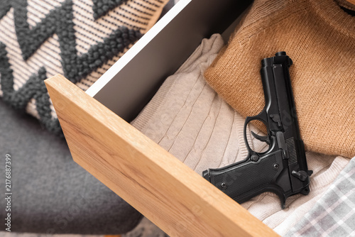 Foto Pistol and clothes in dresser drawer at home, closeup