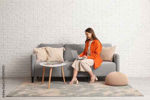 Young pretty woman chatting with laptop on grey sofa at home