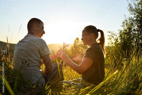 Romantic couple sitting in tall grass holding wild mountain flowers at golden hour sunset, man, woman, love, together