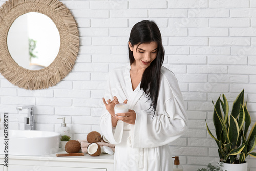 Beautiful young woman applying coconut oil onto hair in bathroom