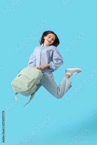 Little schoolgirl with backpack jumping on blue background