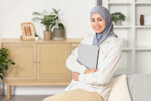 Muslim businesswoman with laptop sitting on sofa at home
