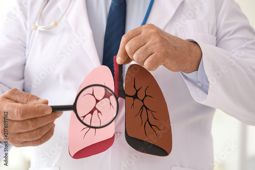 Mature doctor with magnifier and paper lungs in clinic, closeup