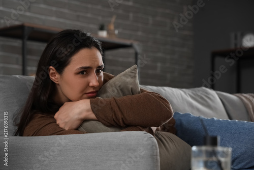 Depressed young woman with pillow lying on sofa at home