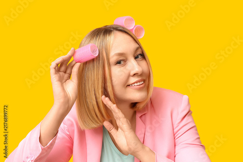 Fotografie Beautiful young woman with bob hairstyle and hair curlers on yellow background