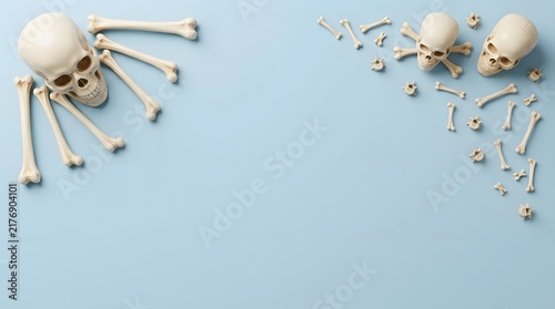Top view of human skulls and scattered bones arranged as a frame on light blue background