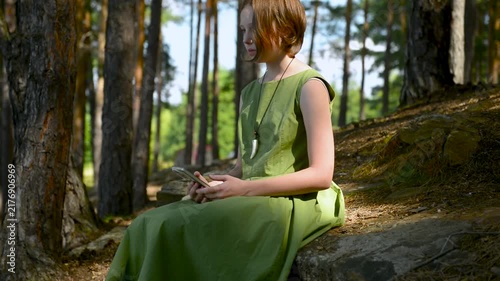 A beautiful summer days. Girl in a green dress sits on among the trees. Summer chill. Golden light. Young woman. Young girl sit among trees in forest. Amazing summer landscape.