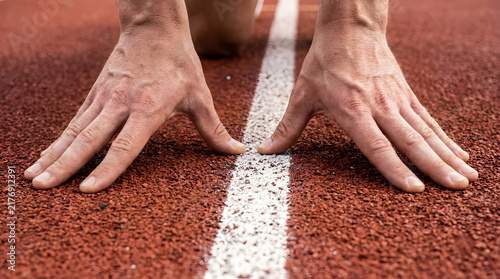 Focused athlete hands poised on the textured red synthetic track surface ready to sprint during a competitive race with intense concentration and determination shown through a low angle close shot.