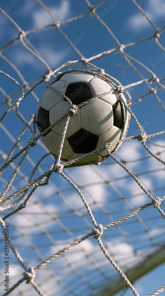 Obraz premium Soccer ball stuck in goal net against blue