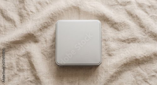 Square metal tin box with lid on a wrinkled beige linen fabric cloth in top view flat lay for mockup design