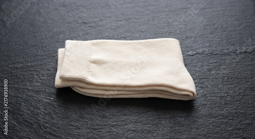 A pair of folded beige cotton socks resting on a dark textured slate background horizontal close up
