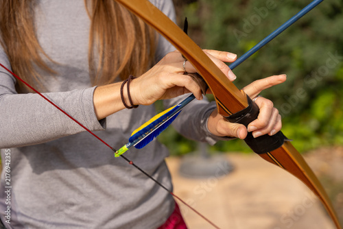 Fotografie Woman's hands placing arrow onto bowstring, preparing for shooting practice outd