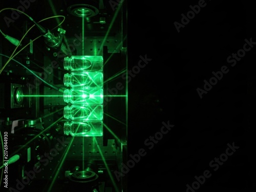 Green laser beam passing through vertical scientific sample column in dark laboratory