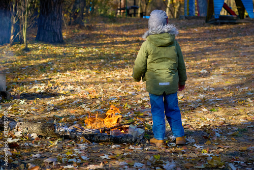 Child in green jacket watches a campfire in a forest park