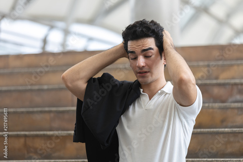 Fotografie Stressed young businessman holding head with eyes closed, carrying suit jacket after difficult workday, expressing fatigue, pressure, frustration, burnout, career stress