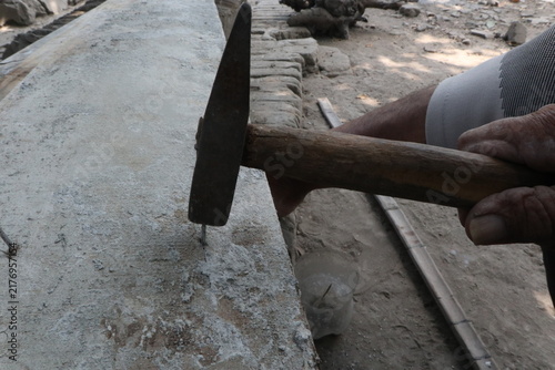 Hammering nail into wooden board. Close-up of a hammer striking a nail into a wooden plank; captures the moment of impact, wood grain, and hands-on carpentry in a rural/workshop setting.