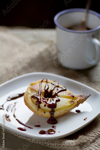 Pear in puff pastry on plate with mug of chocolate sauce, close up