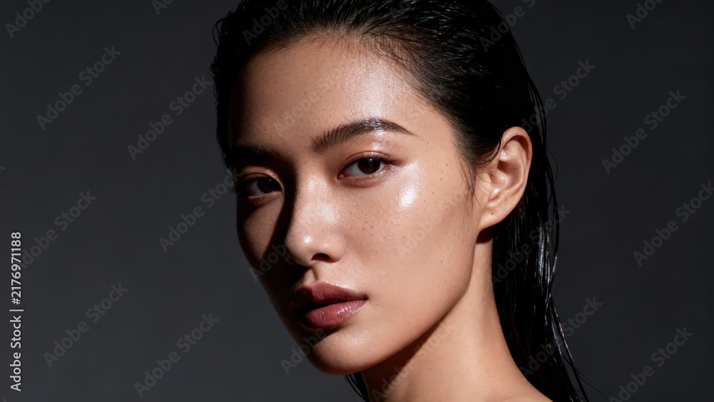 Fototapeta premium Asian female model displaying glowing moist skin closeup studio portrait dramatic dark background beauty care commercial image