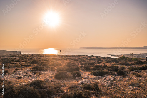 Hilltop panorama with arid landscape, sun shining above the sea and islands on the horizon, Cirkewwa MALTA