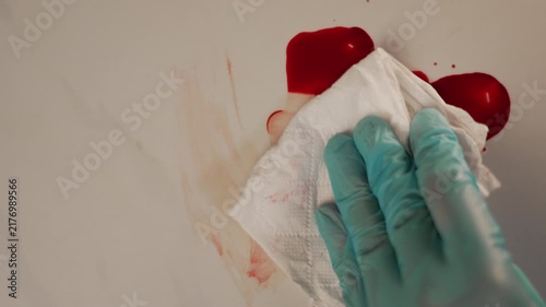 Close up top view of blue gloved hand wiping blood pool with tissue paper, meticulous crime scene sanitation for thriller 