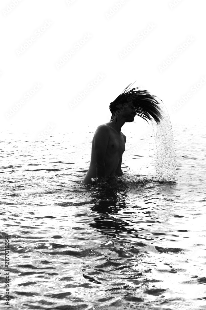 Obraz premium Silhouette of a young man flipping long hair back in sea water, port cranes background