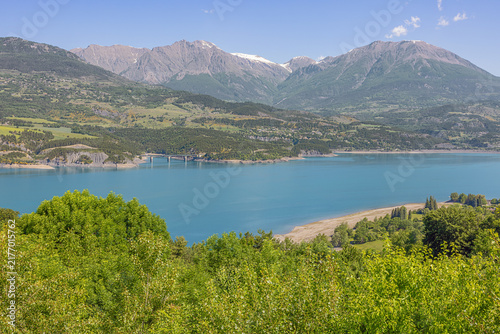 Fotografie Snowcapped mountains above the Lac de Serre Poncon with the bridge over the Riou