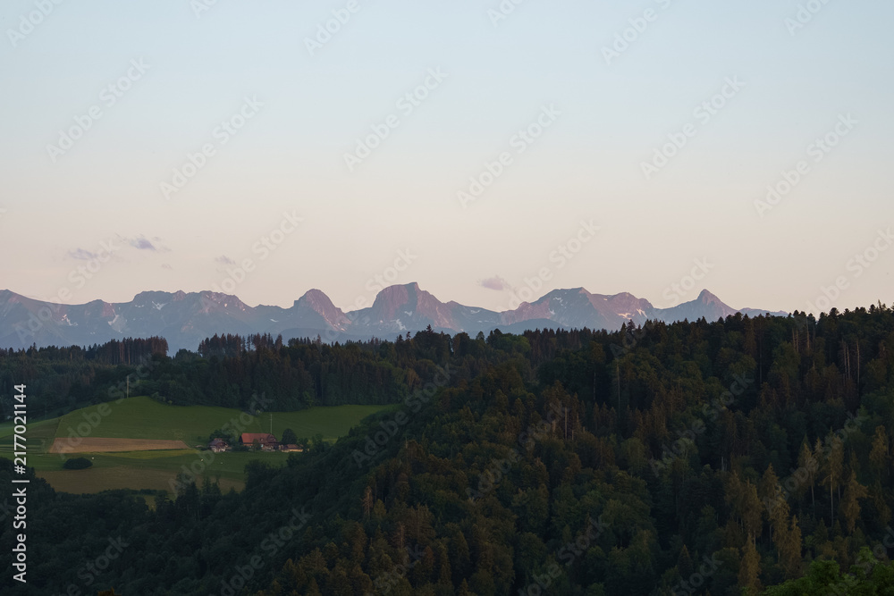 Fototapeta premium Scenic Gantrisch mountain panorama overlooking rolling countryside, forests and agricultural fields beneath a distant Swiss Alps skyline.