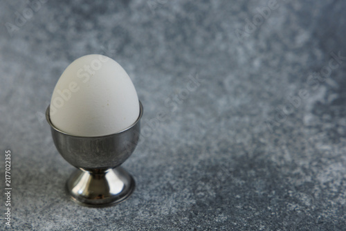 Canvastavla White egg in a metal egg cup on a textured gray surface in a simple kitchen sett