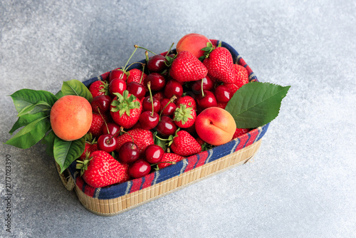 Fresh strawberries and cherries in a basket with apricots on a gray surface during daylight hours
