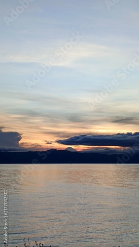 Fotografía Serene Sunset Over Calm Lake and Distant Mountains.