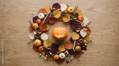 A beautiful autumnal wreath featuring a cute halloween pumpkin surrounded by colorful fall leaves on a rustic wooden background surface