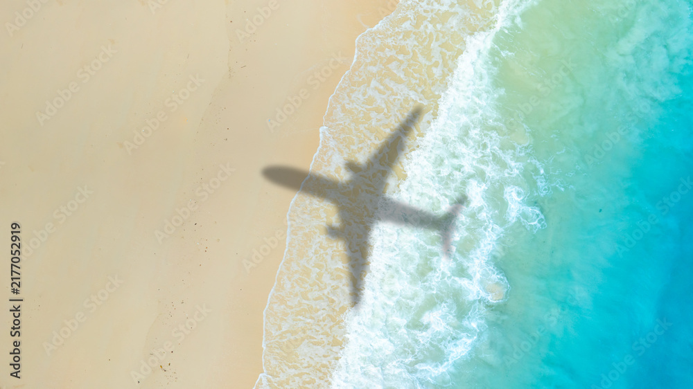 Obraz premium Aerial view of shadow passenger plane silhouette and sandy beach blue sea with waves at sea beach summer vacation sea travel concept 