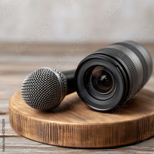 Professional black camera lens and metal microphone placed together on rustic wooden surface symbolizing media production and content creation tools