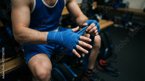 Boxer wrapping hands with blue bandages in locker room, athlete preparing for boxing match, fighter in blue sports uniform